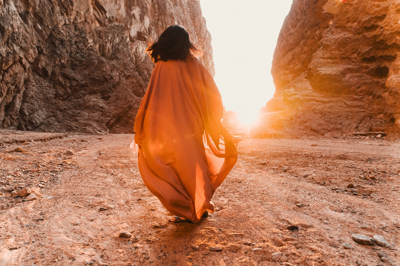 Woman walking toward sunlight between canyon walls
